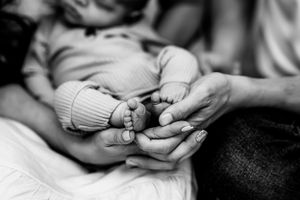 Black and white close-up of tiny newborn feet being gently held by adult hands.