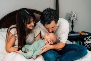 Family sharing intimate moment with newborn baby in mint outfit on bed.