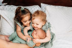 Three siblings in matching mint dresses sharing sweet moment together on white bedding.