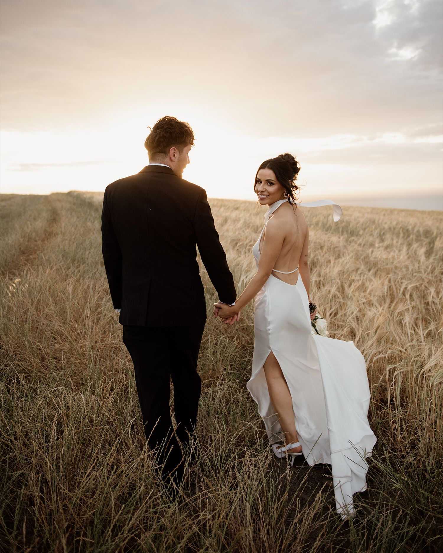 A couple in wedding attire walks through a golden wheat field at sunset, captured in a series of romantic shots.