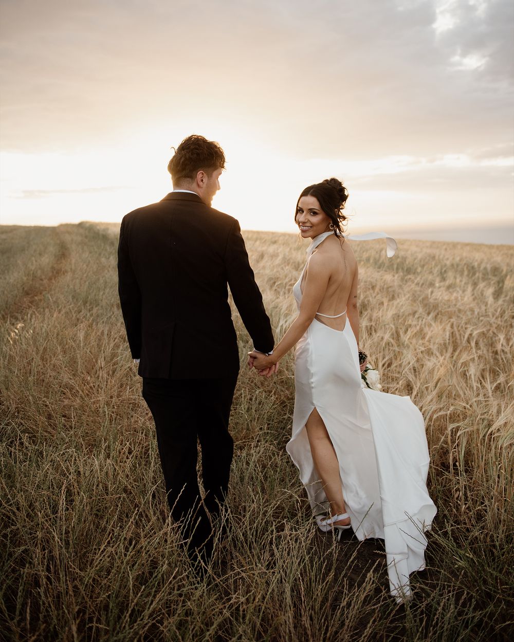 A couple in wedding attire walks through a golden wheat field at sunset, captured in a series of romantic shots.
