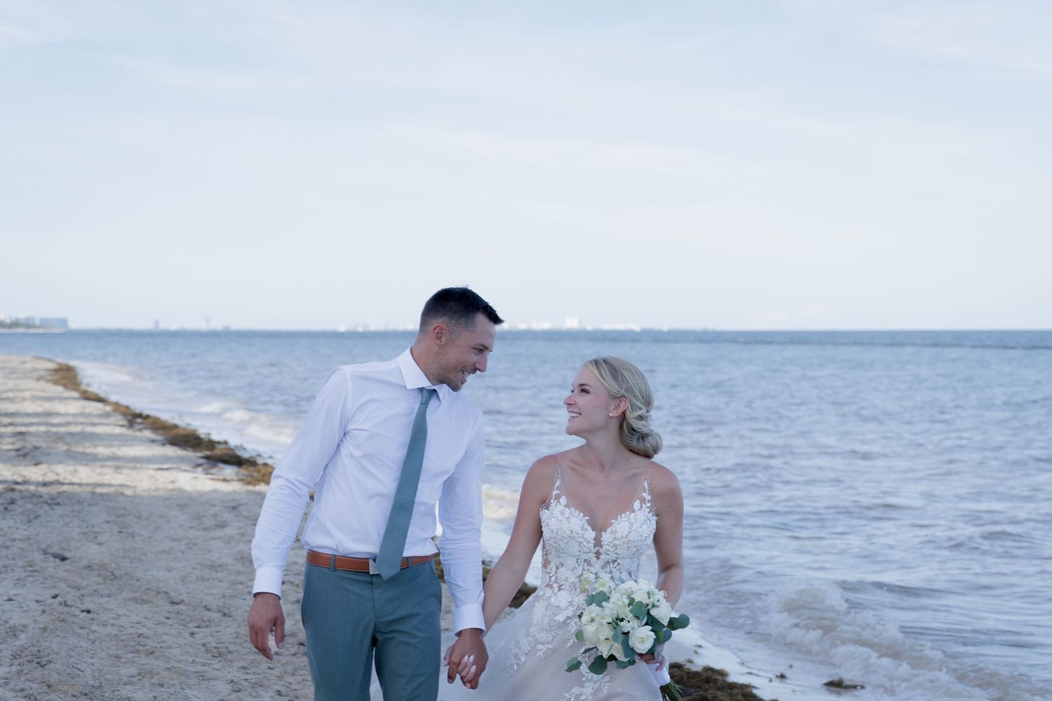 Romantic beach wedding ceremony with floral arch and ocean backdrop at sunset.