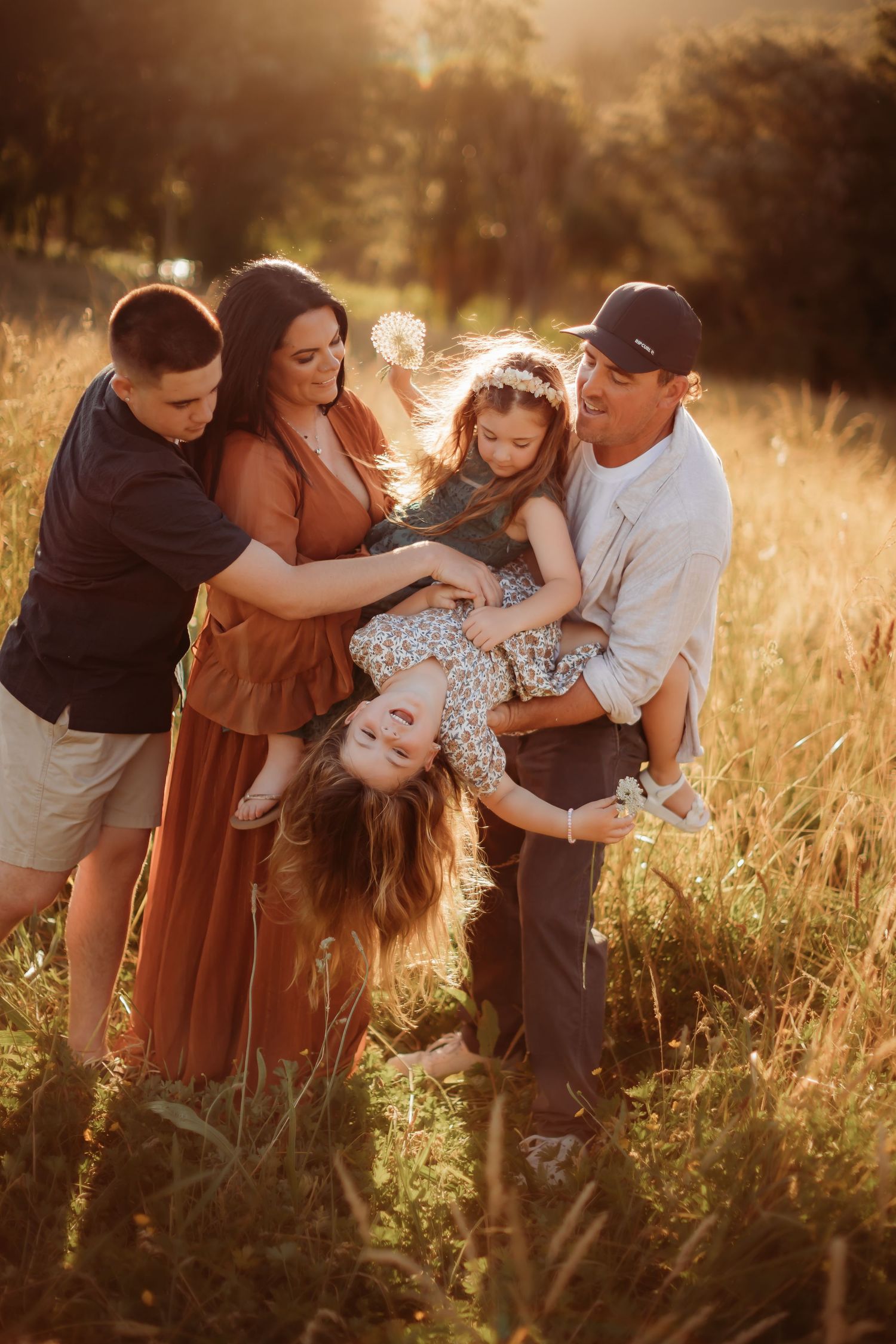 A loving family embraces while sitting together on coastal rocks at sunset.