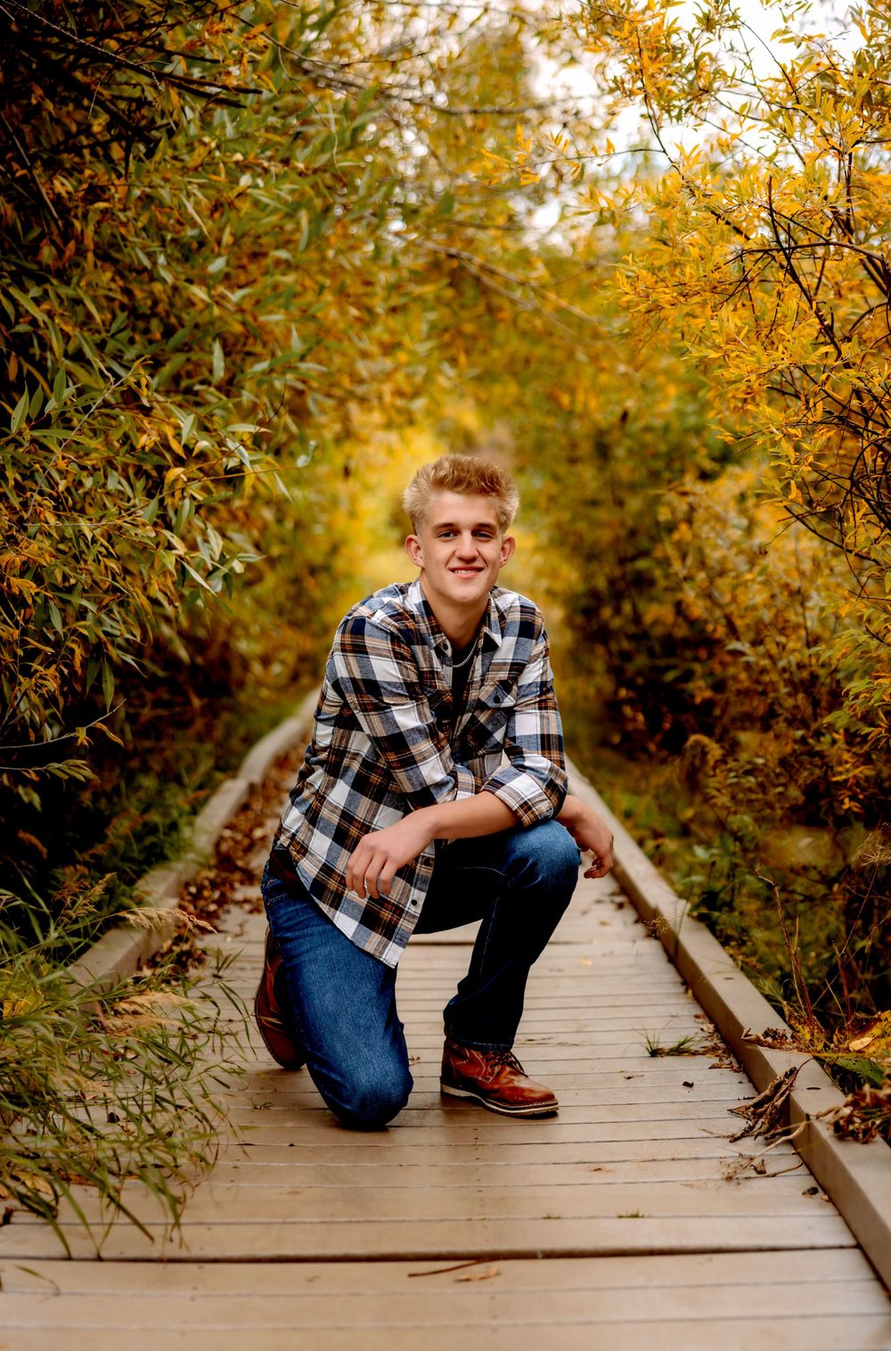Outdoor senior photo session on wooden boardwalk surrounded by autumn foliage in golden light. Senior Pueblo Photographer