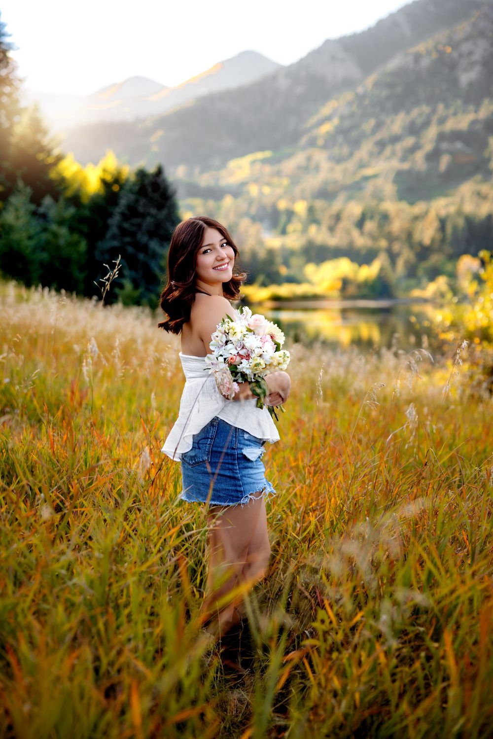 A scenic outdoor photoshoot in a golden meadow with mountains and autumn foliage in the background. Senior Pueblo Photographer