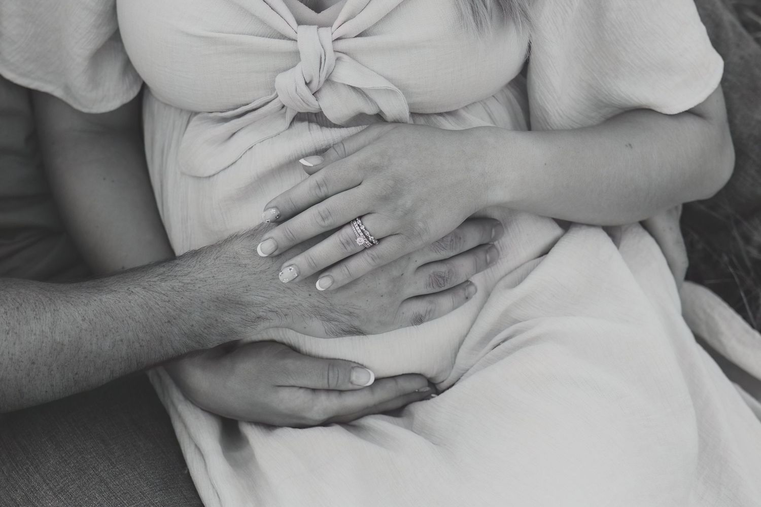 Black and white photo of a pregnant woman with her partner's hands gently cradling her baby bump.