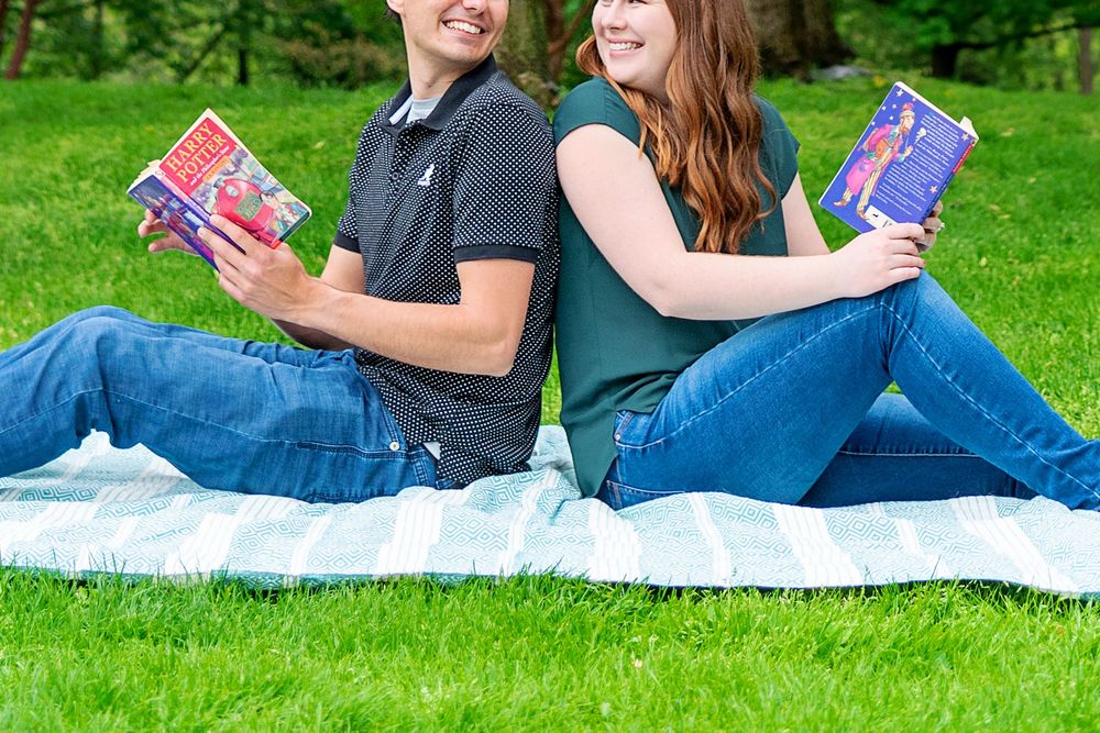 Couple lying on blanket reading Harry Potter books together in a sunny park at Civic Gardens London Ontario.