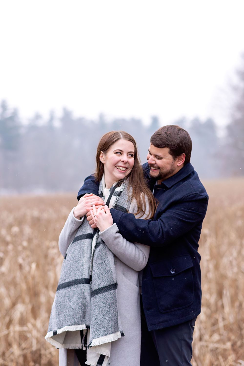 Candid engagement photos in a winter field with muted tones at Springwater Conservation Area.