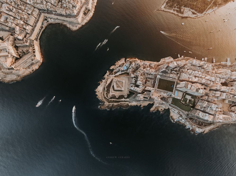 Aerial panoramic view of a coastal Mediterranean city with historic architecture at sunset.
