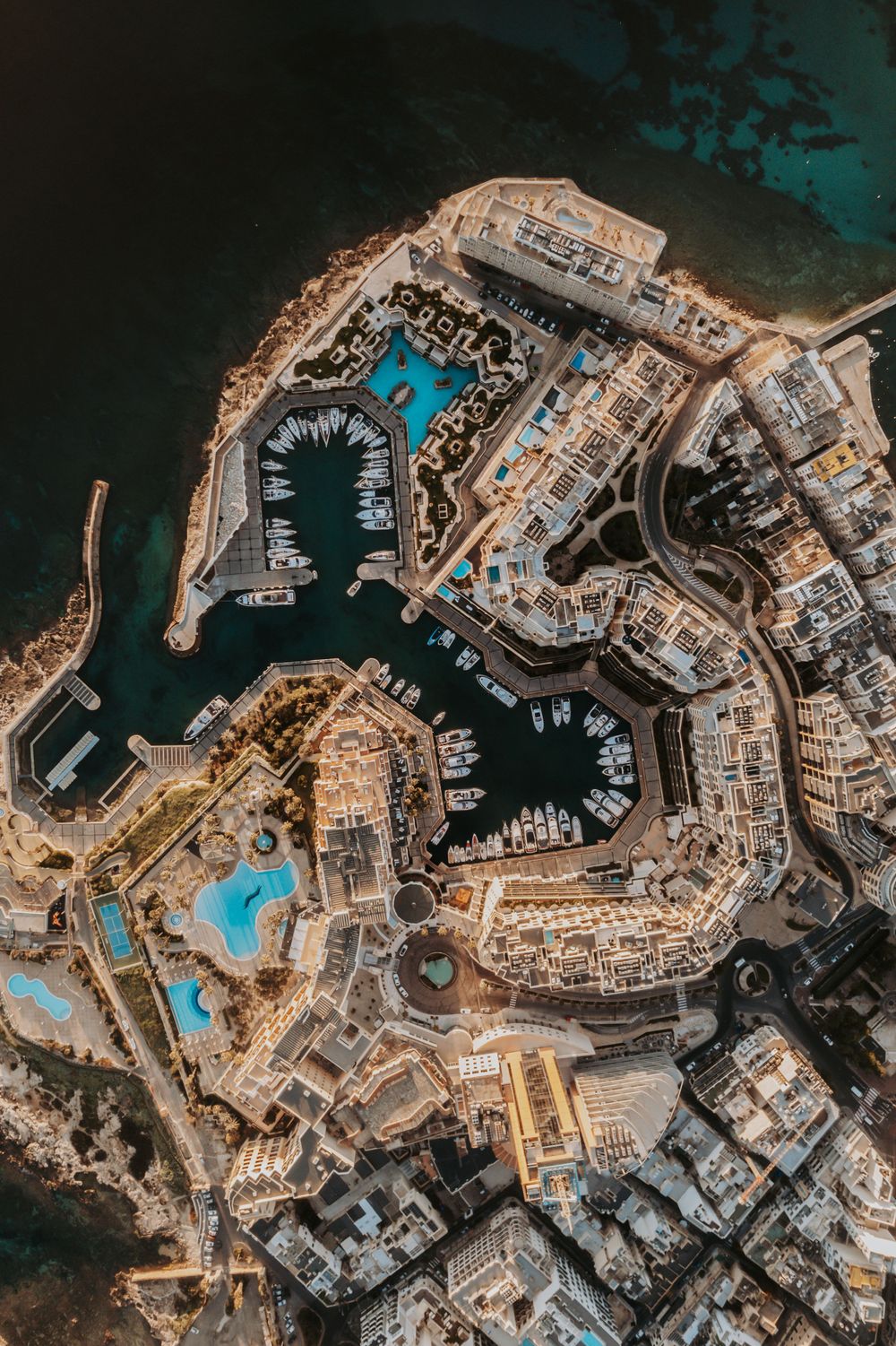 Bird's eye view of a Mediterranean coastal town with turquoise pools and white buildings along the waterfront.