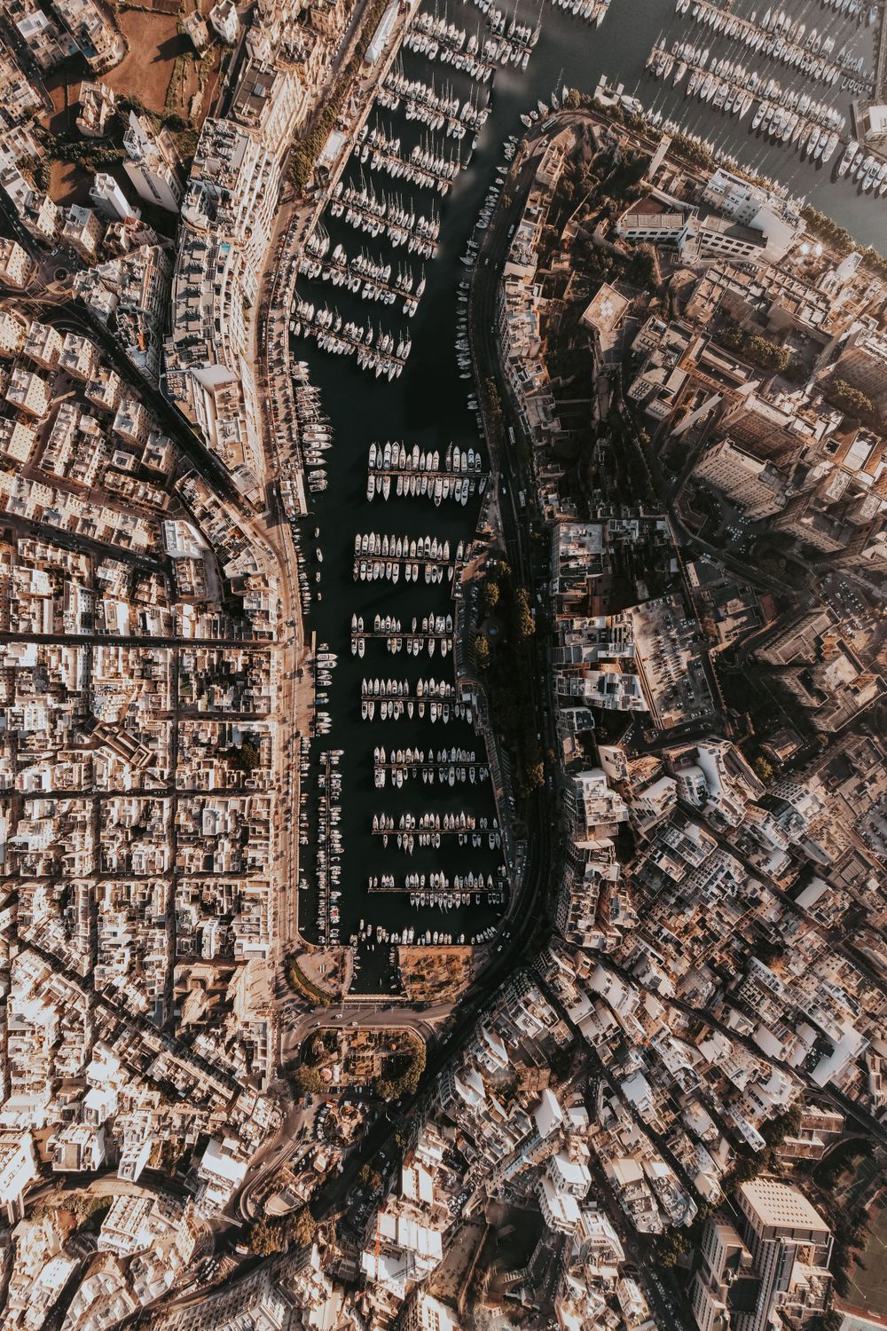 Aerial view of a coastal marina with boats docked in a circular pattern surrounded by urban development.