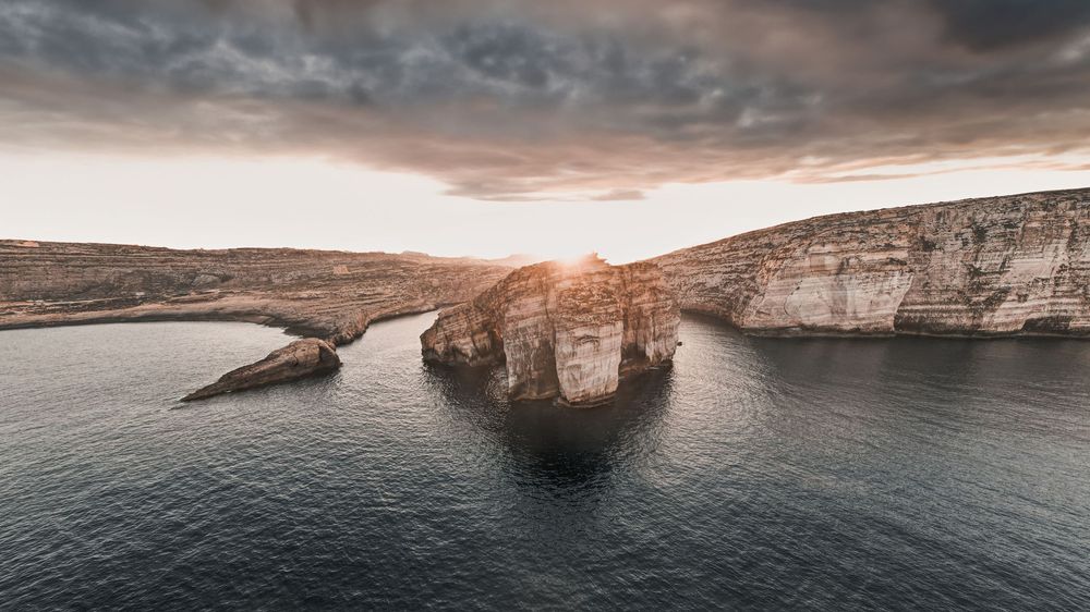 Dramatic coastal landscape with limestone cliffs and natural arch formation at sunset.