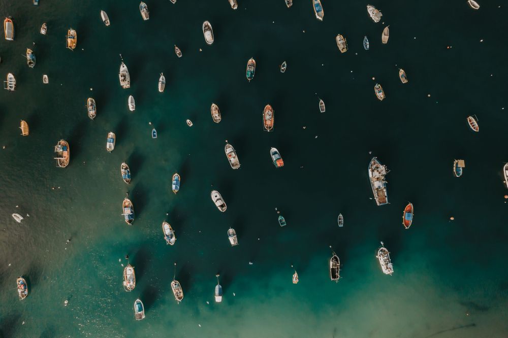 Aerial view of boats anchored in turquoise Mediterranean waters creating a pattern from above.