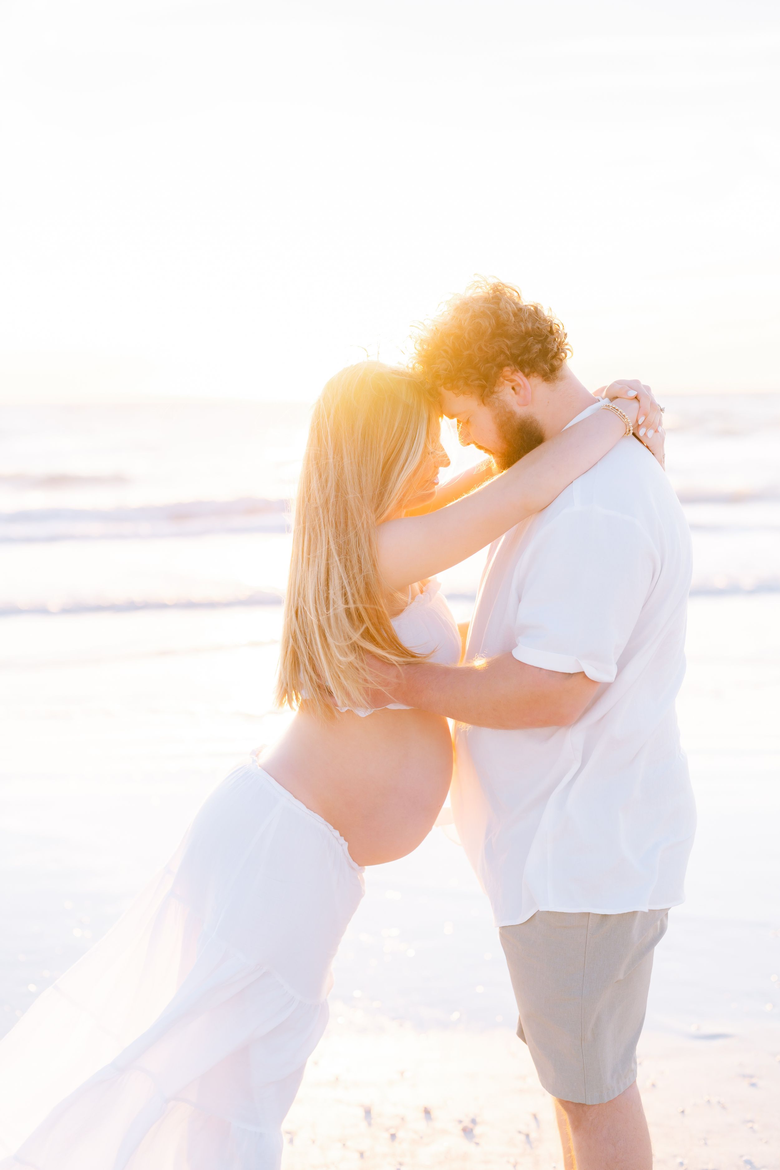 mom and dad embracing on st. Pete beach during their maternity photoshoot at golden hour, Tampa photographer