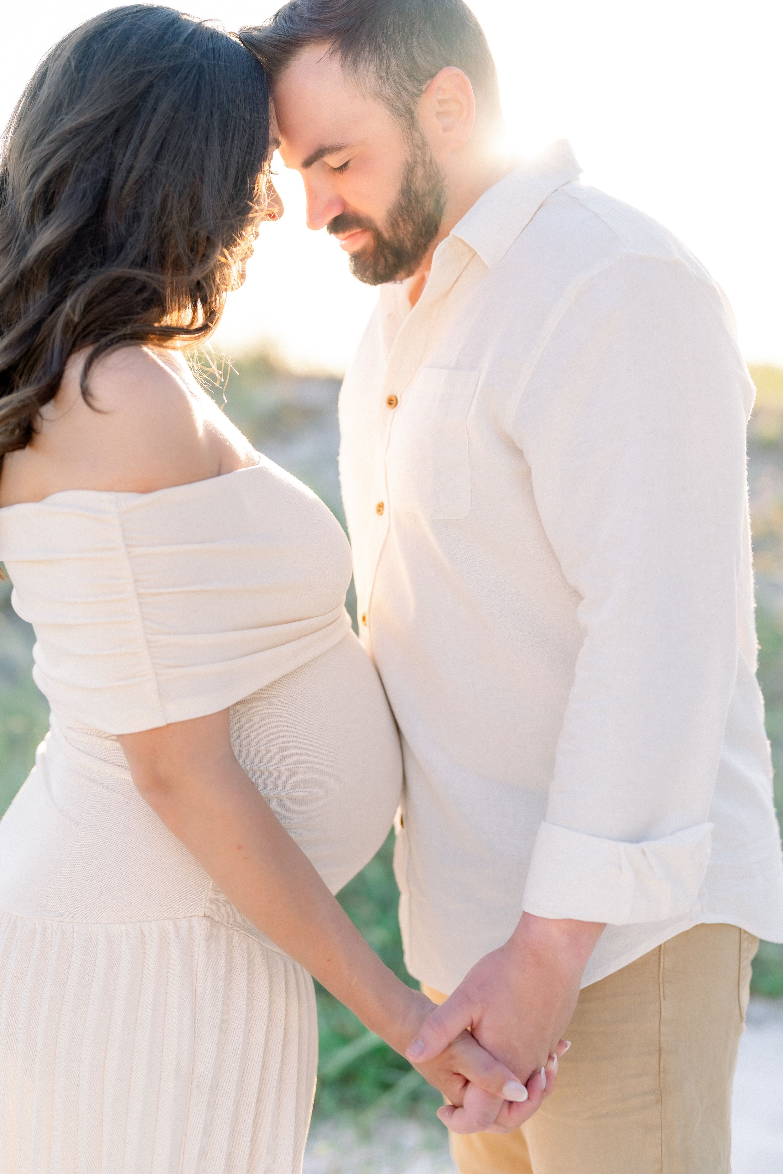 Dad in bliss as he cradles mom hand in hand during their maternity photography session on St. Pete beach at golden hour Don Cesar