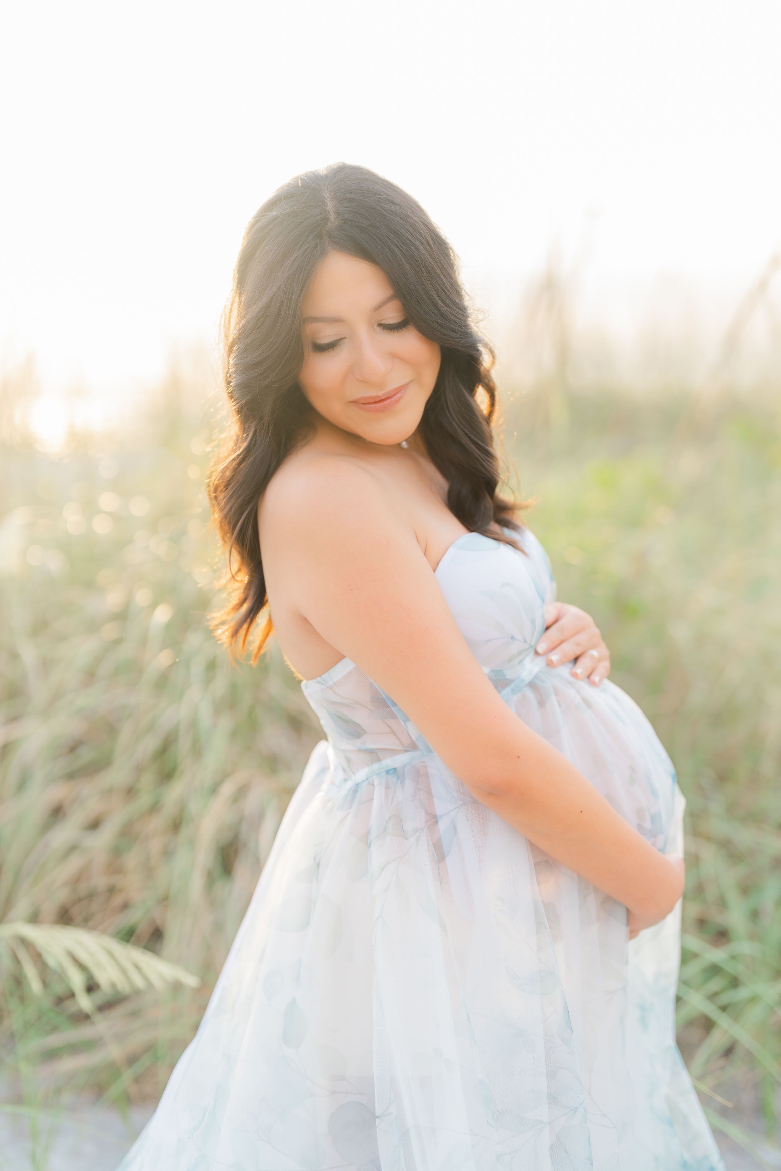 mom holding her belly embracing life during her maternity session at golden hour on St. Pete Beach in Florida