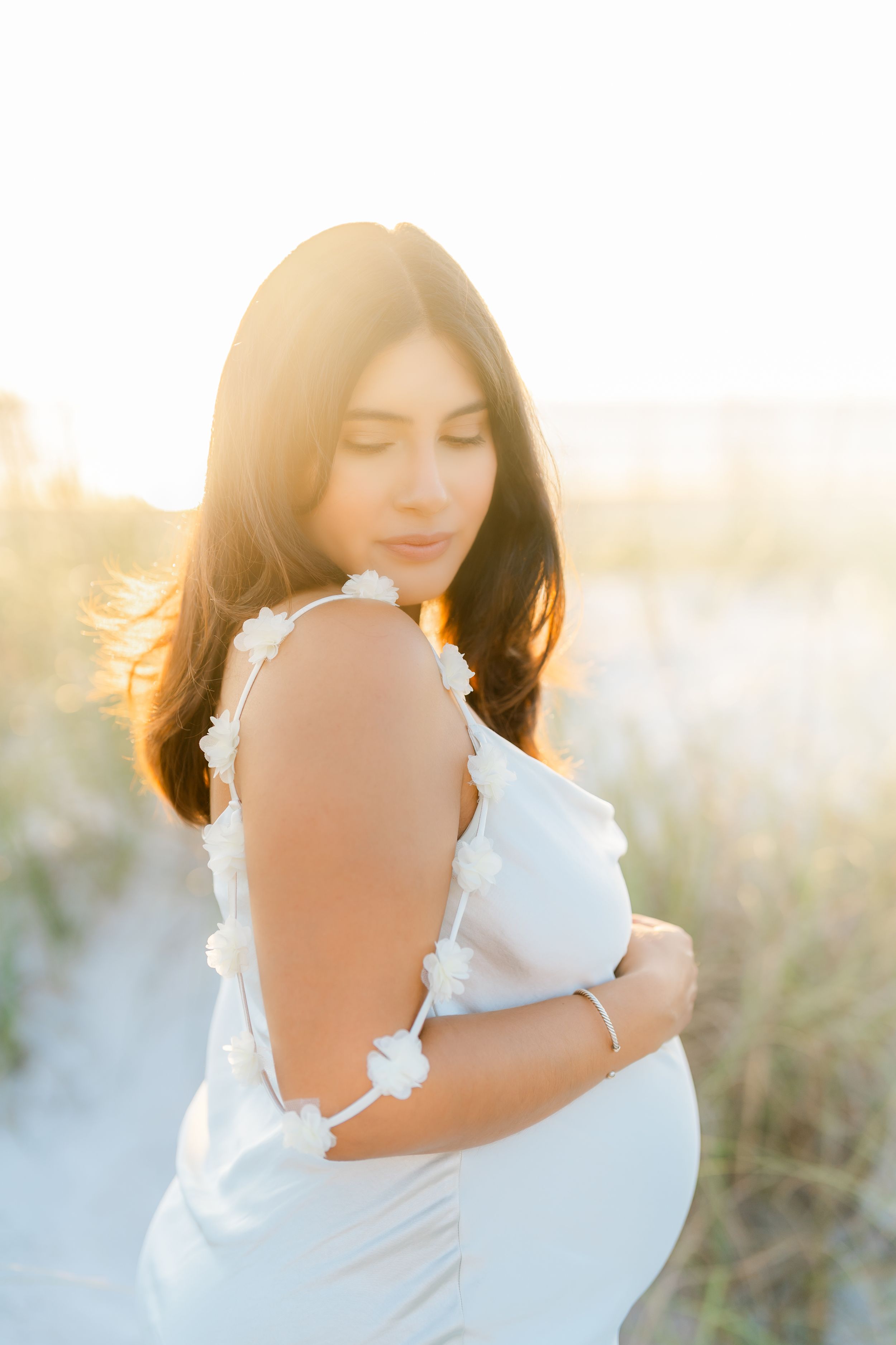maternity photographer in tampa florida, st. Pete beach mom looking down embracing her belly at golden hour