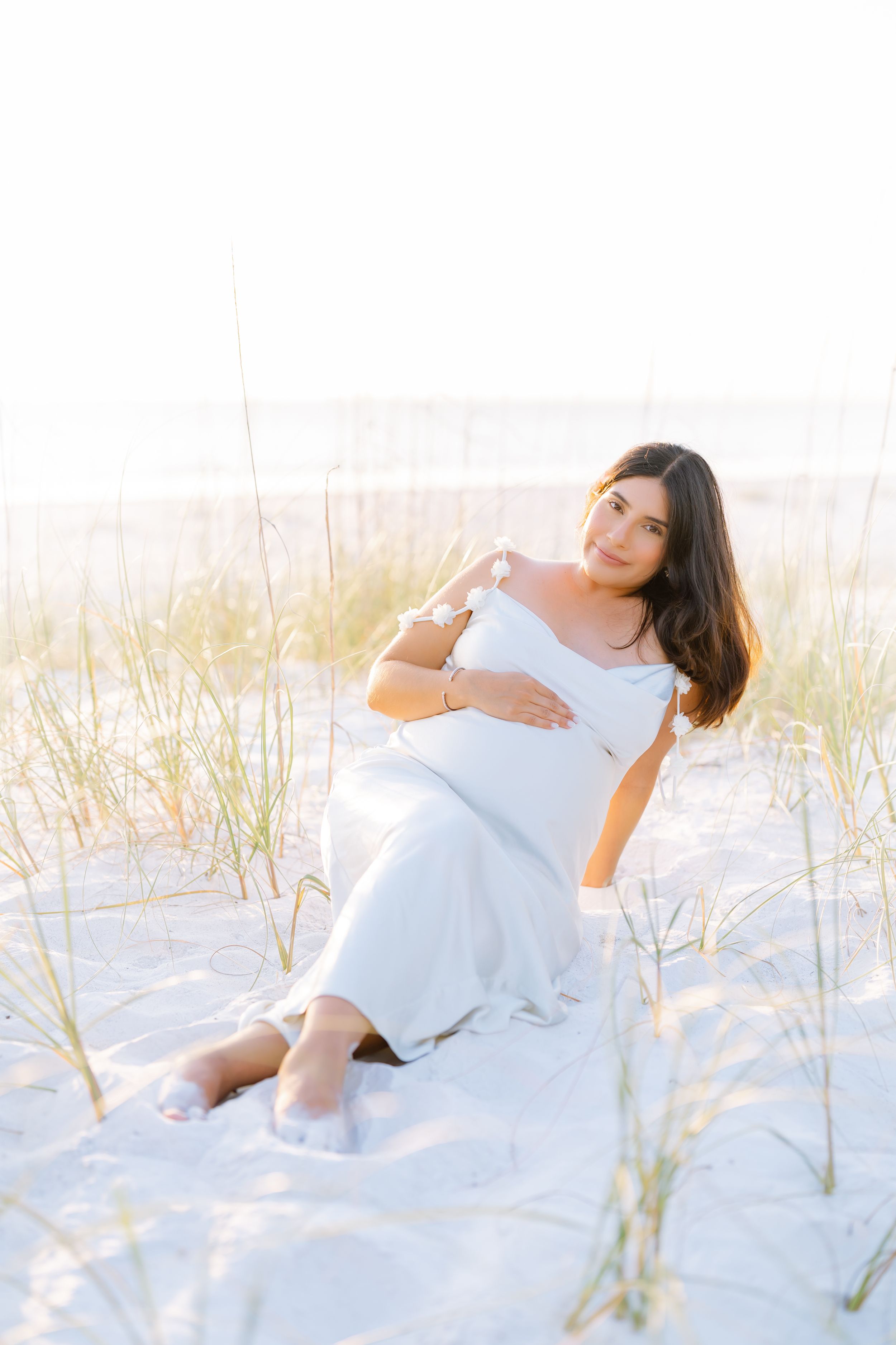 mom laying in sand at golden hour on st. Pete beach florida during her maternity photoshoot by st. Pete photographer
