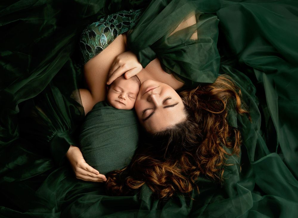 Mother and newborn wrapped in deep green fabric during an intimate maternity and newborn session in Tilton NH