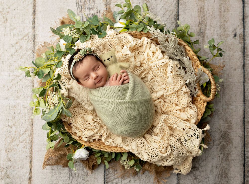 Swaddled newborn resting in a basket with greenery during a studio newborn photography session in Tilton NH