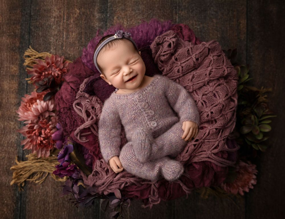 Smiling newborn posed on textured layers with florals during a studio newborn session in New Hampshire