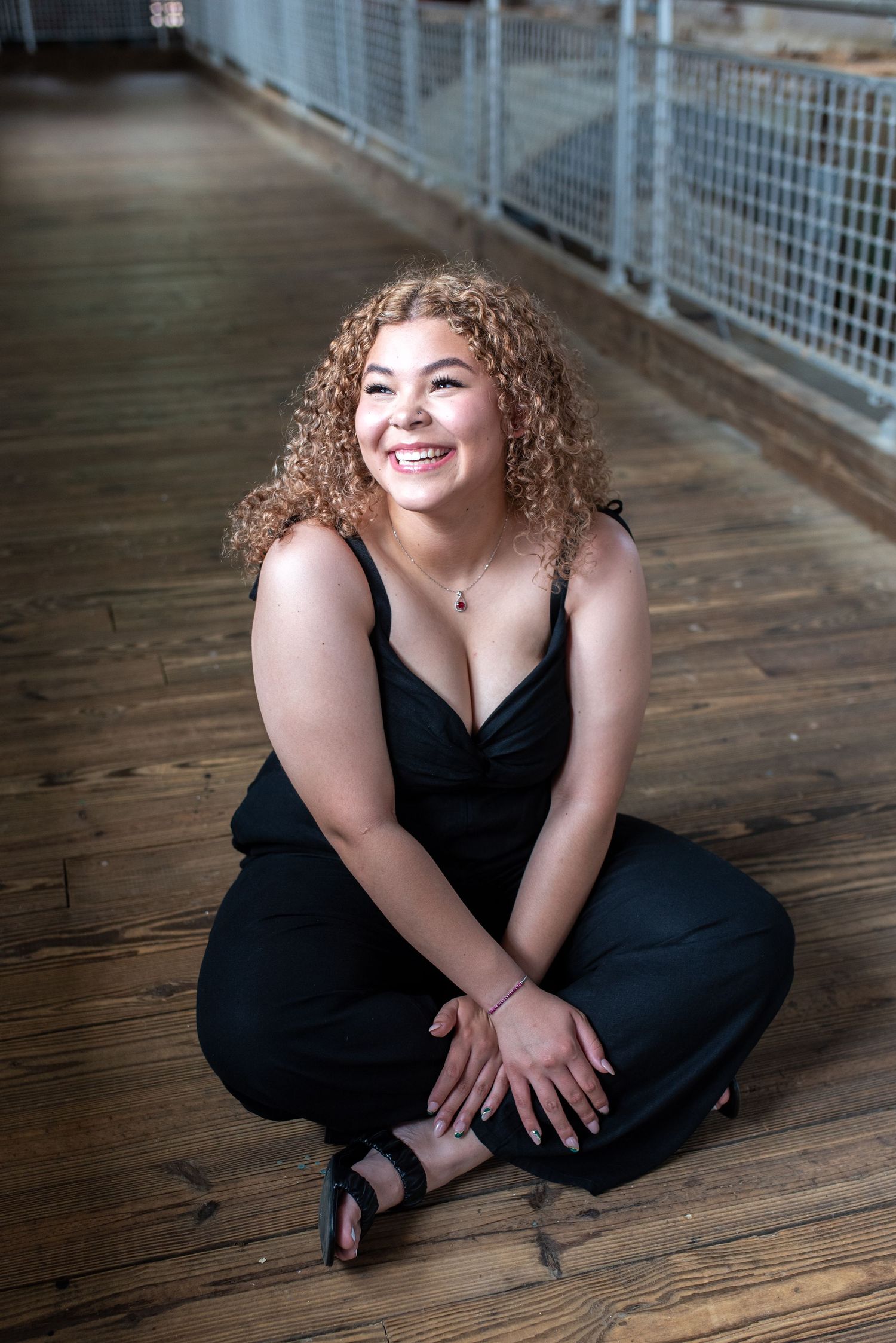 Person in black dress sits on wooden boardwalk during portrait session.