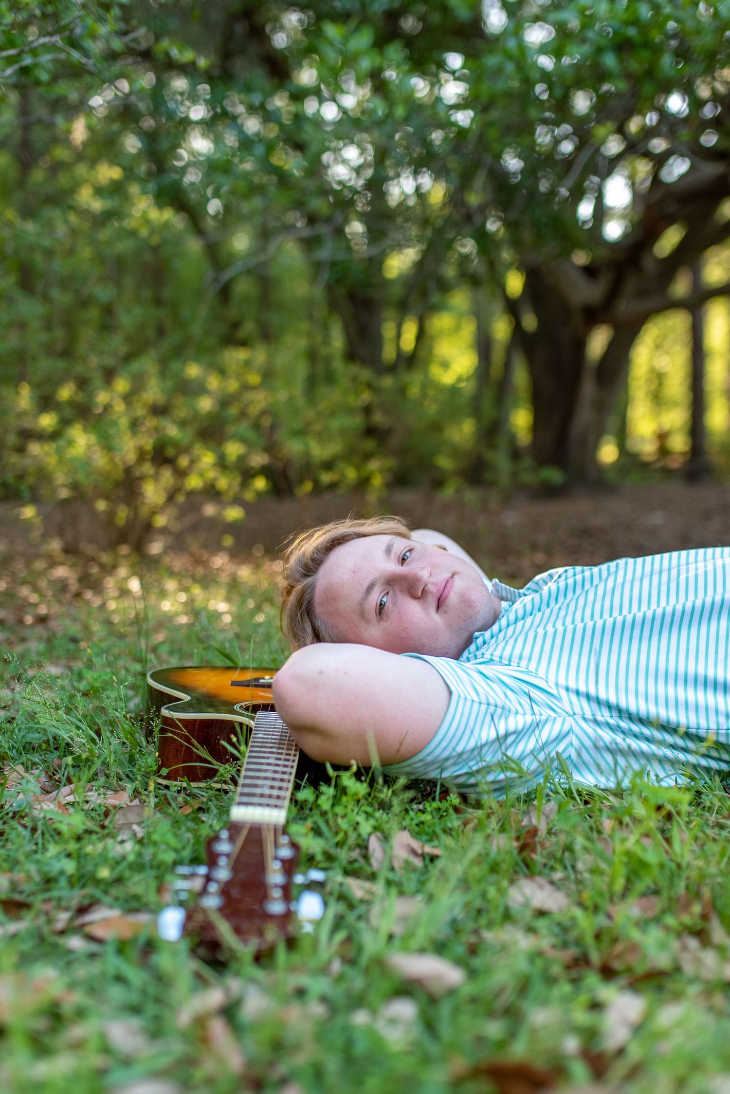 Person lying in grass with guitar during outdoor photo session.