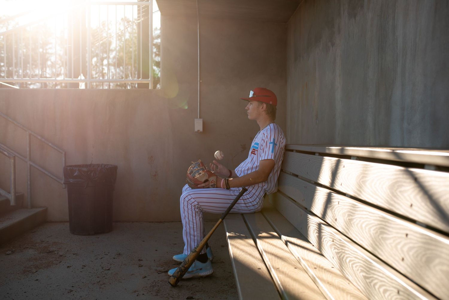 Baseball player sitting in dugout during sunset with dramatic lighting.