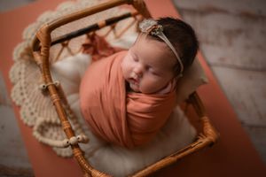 Overhead view of sleeping newborn in peach wrap on vintage wooden prop with lace details.