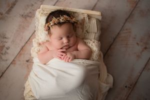 Peaceful newborn sleeping on white fabric with delicate lace accents and floral headpiece.