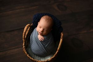 Overhead view of sleeping newborn wrapped in blue swaddle in woven basket.