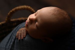 Sleeping newborn in dramatic lighting on textured dark backdrop.