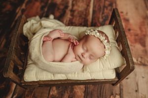 Peaceful newborn sleeping in rustic wooden bed with cream colored bedding.