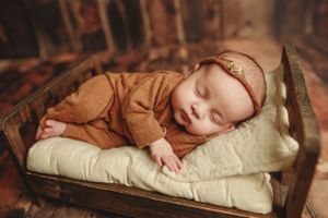 Sleeping newborn wrapped in soft fabrics on rustic wooden bed during professional photoshoot.