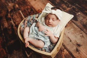 Newborn photography session with baby sleeping in wooden basket on rustic backdrop.