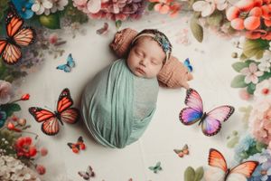 Sleeping newborn wrapped in mint green swaddle surrounded by colorful butterflies and floral decorations.