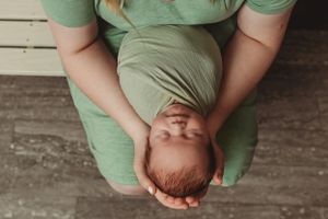 Overhead view of sleeping newborn cradled in caregiver's hands wearing sage green.
