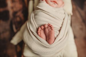 Close-up of tiny newborn feet peeking out from white textured swaddle wrap.