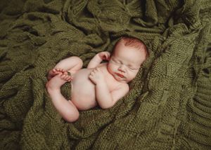 Sleeping newborn lying on olive green knit blanket during professional photo session.