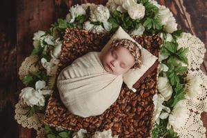 Newborn photography setup with white flowers and greenery arranged in circular pattern.