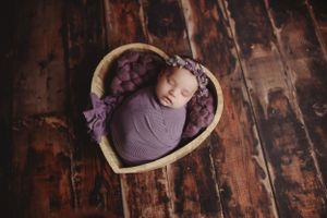 Artistic newborn portrait on dark wooden floor with purple fabric accents.