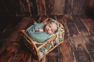 Newborn photography in vintage-style wicker basket on rustic wooden floor.