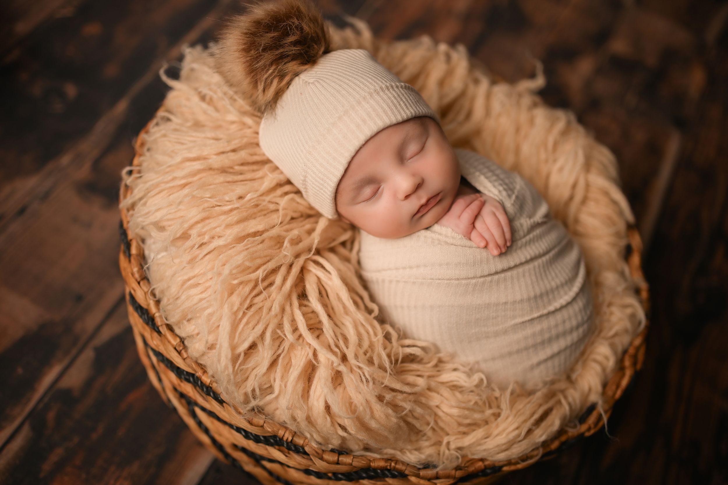 Peaceful sleeping baby wrapped in cream swaddle on fluffy tan nest.