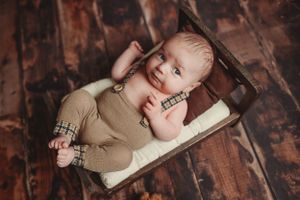 Newborn in beige outfit sleeping on rustic wooden surface during photo session.