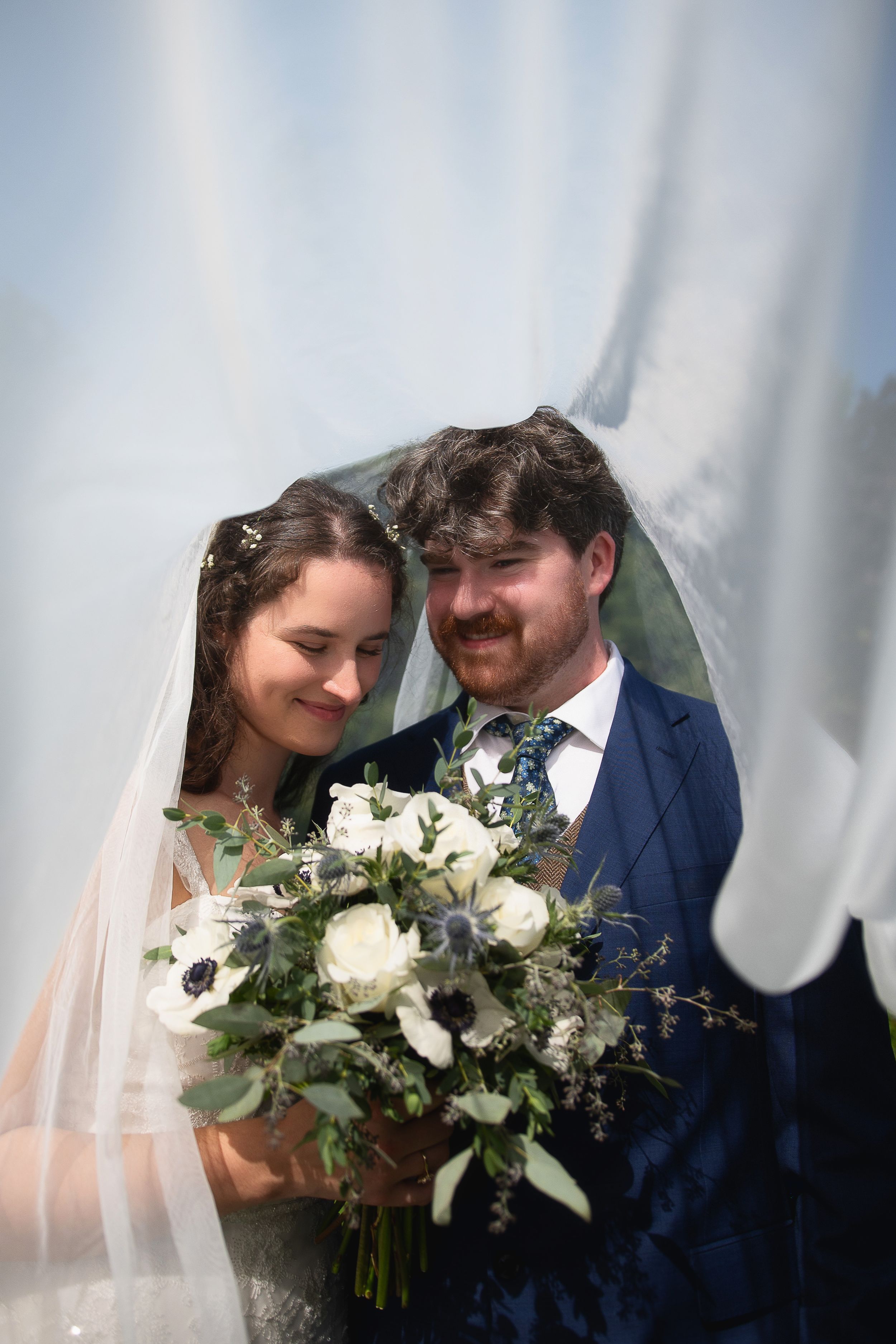 A happy couple shares an intimate moment on their wedding day with a beautiful white and green floral bouquet.