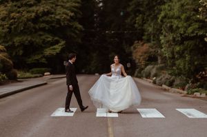 A couple in wedding attire walks through a lush garden path holding hands during their outdoor ceremony.