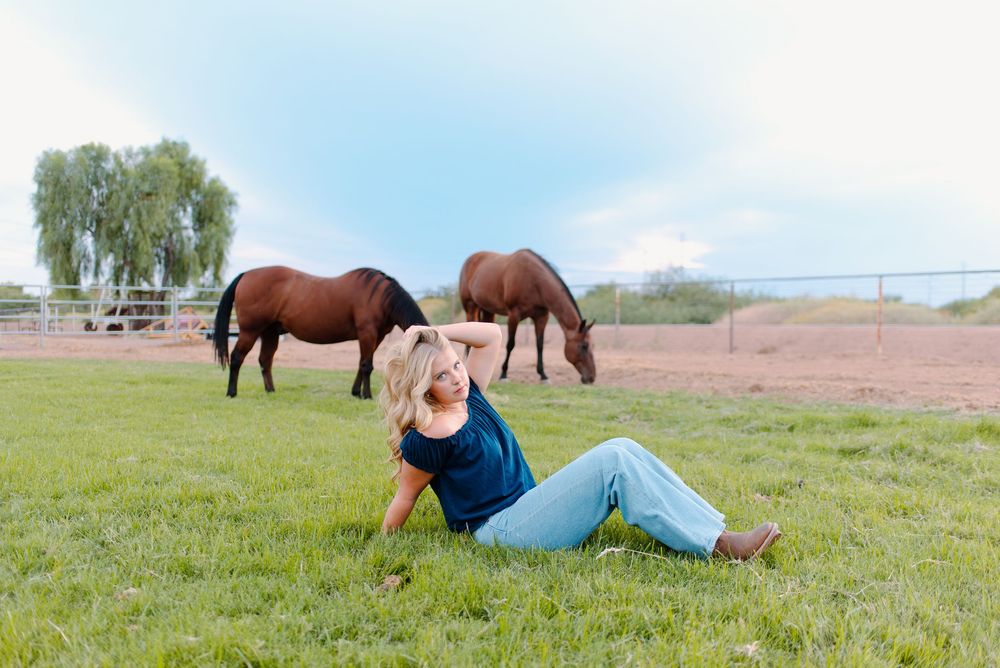 Photo of a high school senior at her senior photos in Gilbert, Arizona in a pasture setting with horses.