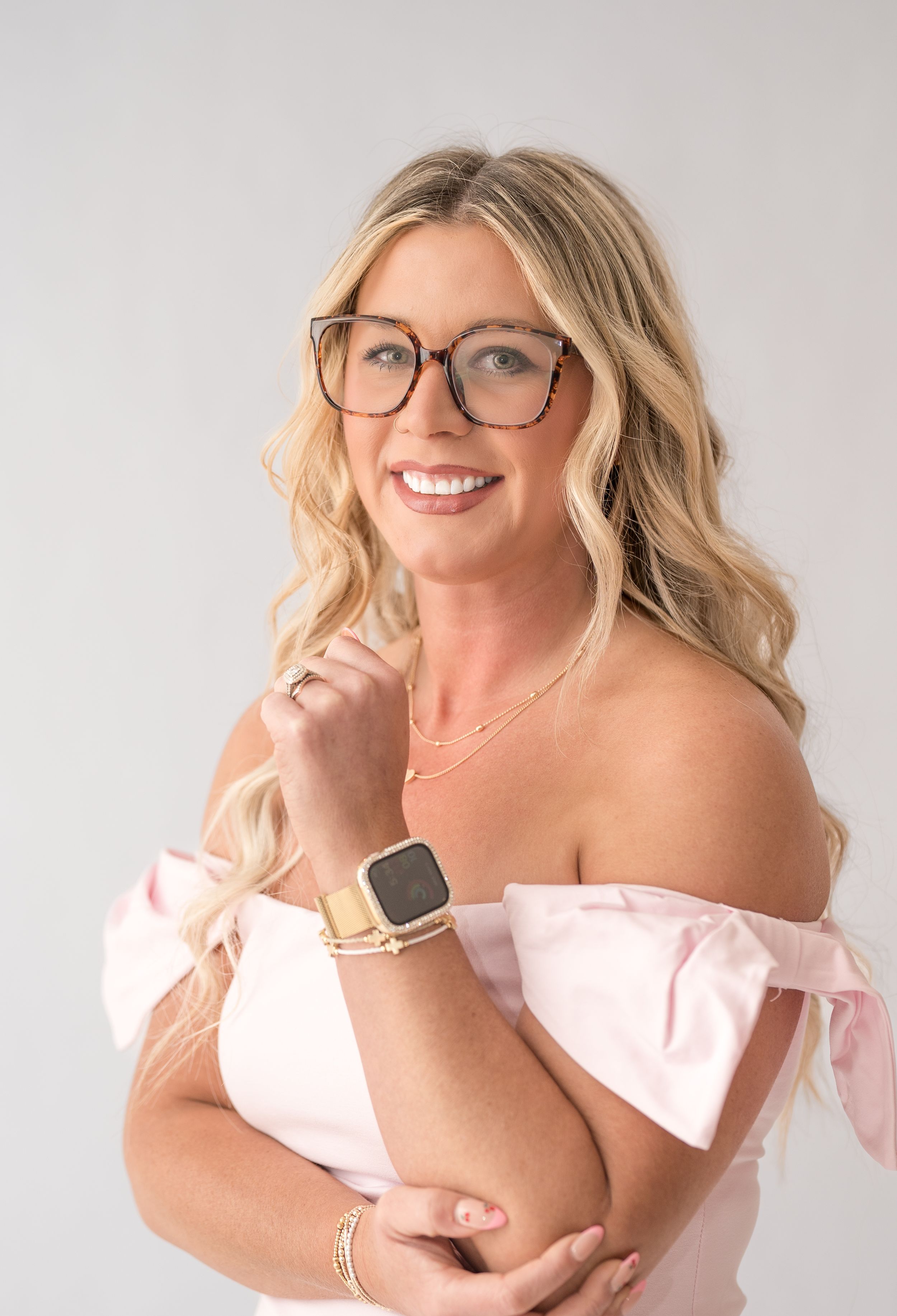 Portrait series in pink off-shoulder top with makeup brushes against grey background.