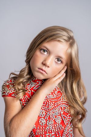 A young child in a red and white polka dot dress poses expressively with blonde hair against a light background.