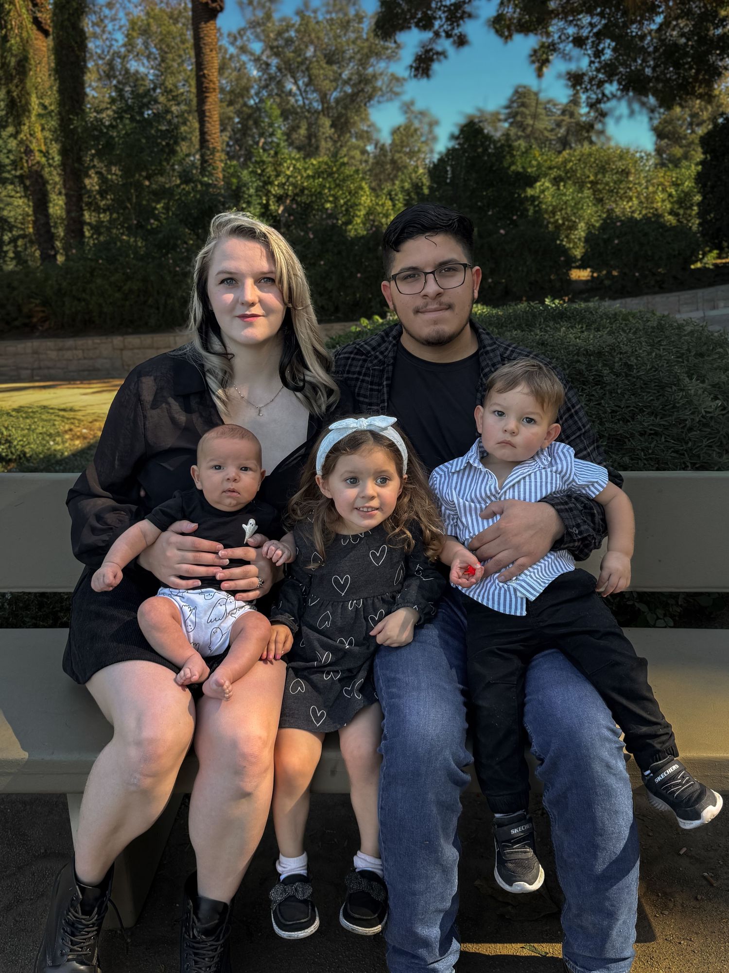 Family sitting together on a park bench during golden hour surrounded by trees and greenery.